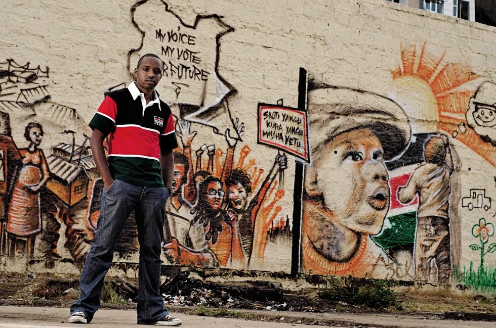 Boniface Mwangi Posing in front of the first Wall Graffiti on Muindi Bingu Street, Nairobi Boniface Mwangi Posing in front of the first Wall Graffiti on Muindi Bingu Street, Nairobi